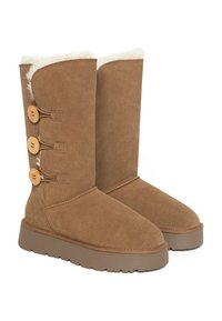 Botas altas de ante marrón con un forro blanco esponjoso, tres botones grandes, una suela texturizada y un diseño de punta redondeada.
