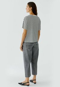 Gestreiftes Schwarz-Weiß-Shirt mit kurzen Ärmeln, kombiniert mit grauen weiten Jeans und schwarzen Slingback-Schuhen. Einfaches, lässiges Outfit.