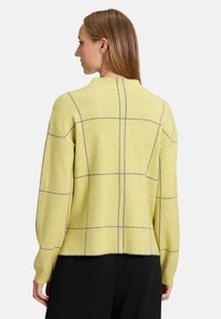 Żółty sweter z szarym wzorem w kratę, luźny krój, ściągacze przy mankietach i dekolcie, miękka tekstura i lekko skrócony dół.