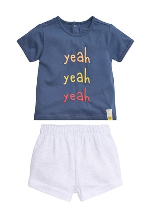 Camiseta de manga corta para niño pequeño en azul marino con el texto "yeah yeah yeah" en naranja, amarillo y rojo, combinada con pantalones cortos blancos con cintura elástica.