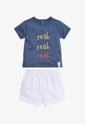 Camiseta de manga corta para niño pequeño en azul marino con el texto "yeah yeah yeah" en naranja, amarillo y rojo, combinada con pantalones cortos blancos con cintura elástica.