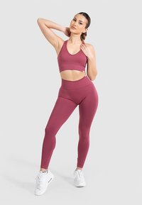 Sujetador deportivo granate y leggings de talle alto con textura acanalada, combinados con zapatillas blancas. Diseño simple con detalles recortados en la cintura.