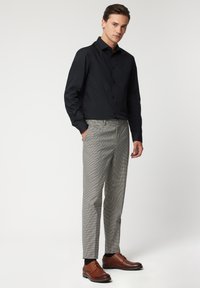 Czarna koszula na guziki, szare spodnie w kratę i brązowe skórzane buty. Koszula ma dopasowany krój, a spodnie mają prostą nogawkę.