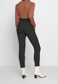 Brown knit sweater with a round neckline paired with high-waisted, dark gray tailored pants and white ankle boots with a block heel.