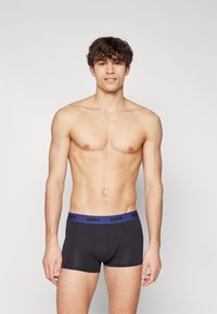 Sorte boxershorts med en marineblå elastisk linning som har merkevarenavnet "DIM." Stoffet ser glatt og tettsittende ut.