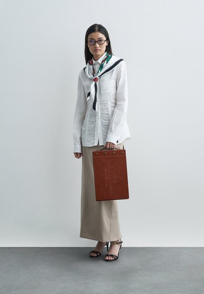 Kvinde iført briller, hvid rynket skjorte med et farverigt tørklæde, beige nederdel, sorte hæle, og holder en brun læder tote taske.