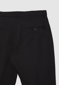 Pantaloni neri in tessuto strutturato, con una tasca posteriore con chiusura a bottone e due tasche a filetto, design a vestibilità sagomata.