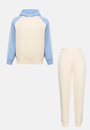 Κρέμ φούτερ με κουκούλα και ανοιχτό μπλε μανίκια raglan, μαζί με ταιριαστά κρέμ παντελόνια jogging με ανοιχτό μπλε ρίγες στο πλάι, παρουσιασμένα σε απλό φόντο.