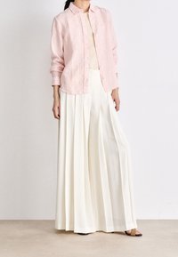 Różowa koszula z paskami, zapinana na guziki, zestawiona z kremowymi spodniami typu wide-leg, prezentującymi luźny krój i miękką fakturę materiału. Całość dopełniają czarne sandały.