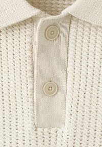 Polo in maglia color crema con motivo a trama e due bottoni beige sulla patta sotto il colletto.