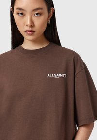 Camiseta de gran tamaño color marrón, hecha de algodón, con cuello redondo y "ALLSAINTS LONDON" estampado en blanco en el pecho.