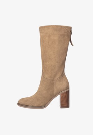 Botte haute jusqu'au genou en daim beige avec talon bloc, bout arrondi et languette latérale. Texture lisse avec des détails de couture minimaux.