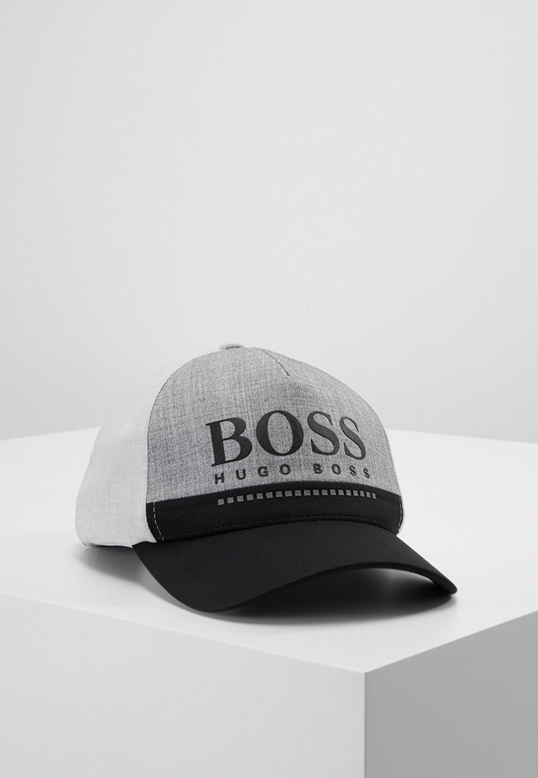 Casquette de baseball grise et blanche avec une visière noire, avec le logo "BOSS HUGO BOSS" sur le panneau avant, posée sur une surface blanche.