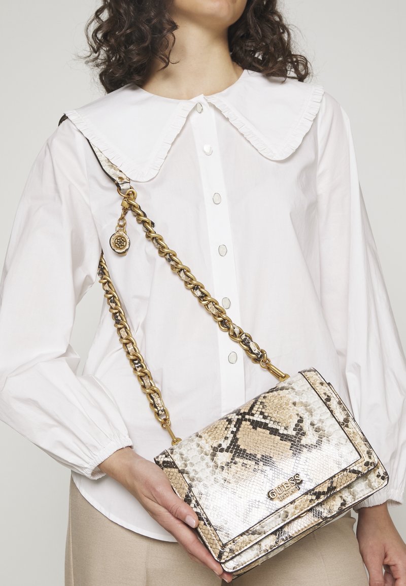 Borsa a tracolla con motivo in pelle di serpente beige e nera, dotata di una catena dorata, chiusura con gancio e dettaglio logo sul davanti.