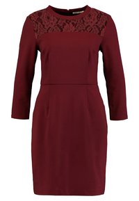 Bordowa sukienka z długimi rękawami, koronkowym panelem na ramionach, dopasowaną górą i usztywnioną spódnicą. Zamek z tyłu. Rozciągliwy materiał.