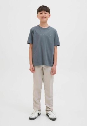 Camiseta de algodón gris con cuello redondo y estampado de logo en blanco. Se combina con pantalones beige claros y sneakers en blanco y negro.