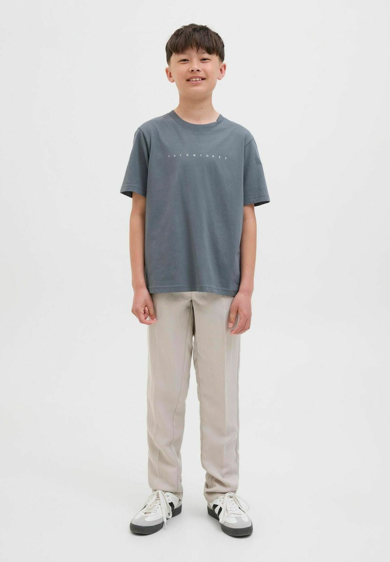 Camiseta de algodón gris con cuello redondo y estampado de logo en blanco. Se combina con pantalones beige claros y sneakers en blanco y negro.