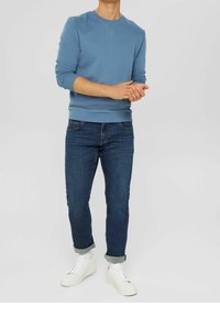Sudadera azul claro de manga larga, combinada con jeans azul oscuro y zapatillas blancas. El conjunto tiene un corte holgado y los puños enrollados.