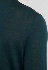 Turkusowy sweter dzianinowy z prążkowaną teksturą i dopasowanym krojem. Widoczne szwy na ramionach oraz gładkie wykończenie materiału.