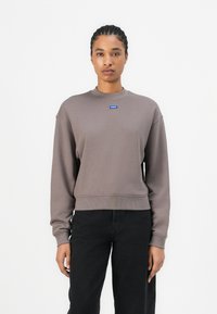 Brown cropped sweatshirt with a crew neck, ribbed cuffs, and hem; features a small blue logo on the chest; smooth texture.