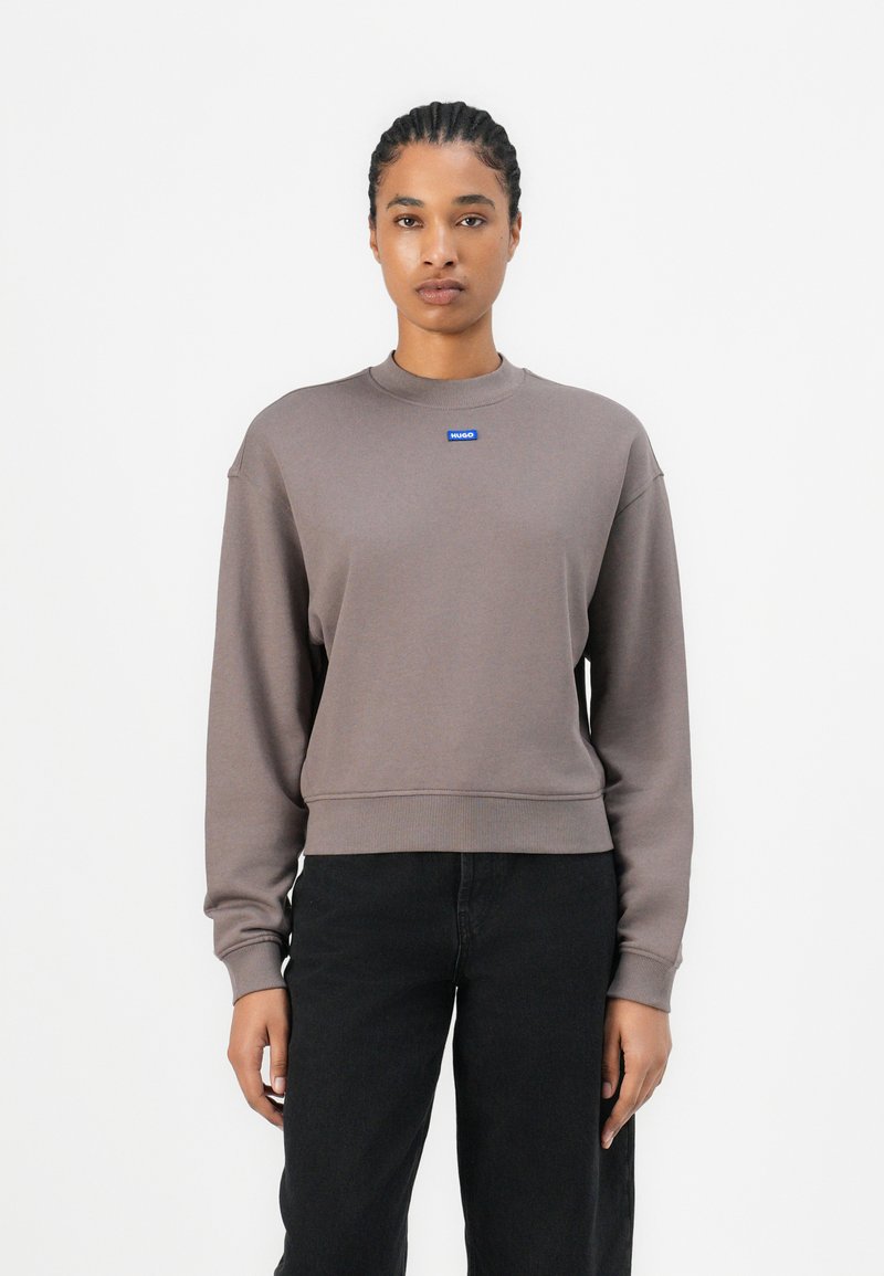 Brown cropped sweatshirt with a crew neck, ribbed cuffs, and hem; features a small blue logo on the chest; smooth texture.