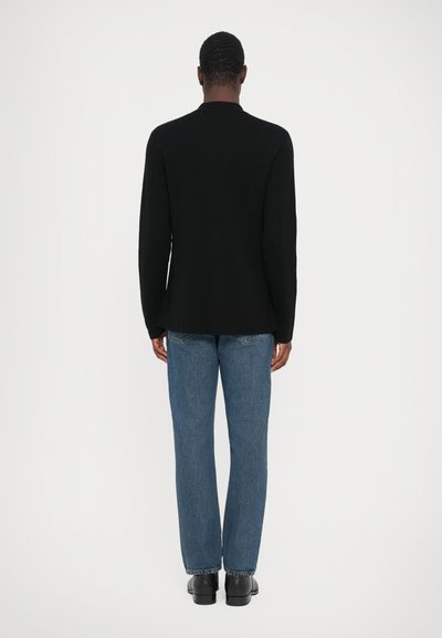Zwarte langemouwen top met een rechte snit, gecombineerd met blauwe denim jeans. De stof lijkt glad, met een eenvoudig kraagontwerp.