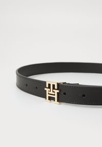 Schwarzer Ledergürtel mit glatter Textur und goldfarbener Logosschnalle mit ineinandergreifenden Buchstaben. Fünf verstellbare Löcher für die Größe.