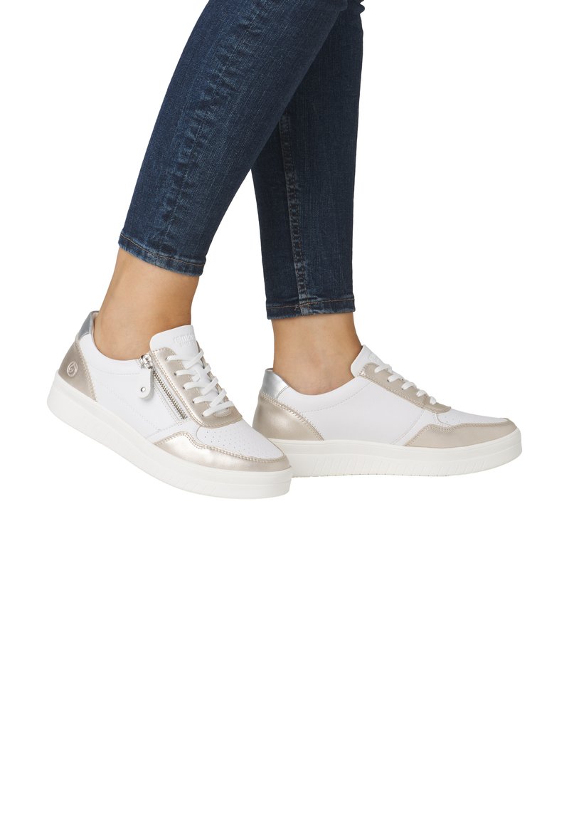 White and metallic silver sneakers with textured accents, lace-up front, zip detail on the side, and a rubber sole, worn with dark jeans.