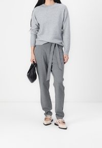 Pull en tricot gris à col rond, associé à un pantalon gris avec une taille nouée. Sac à main noir et chaussures beiges avec des accents.