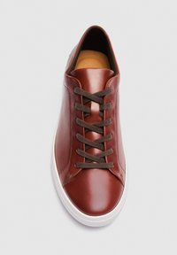 Baskets en cuir marron avec des lacets marron foncé et une semelle en caoutchouc blanche, vues de dessus sur fond blanc.