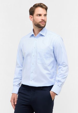 Camicia azzurro chiara con bottoni, motivo a righe verticali, taschino sul petto e maniche lunghe. Il tessuto sembra liscio e leggero.