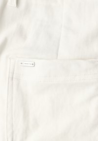 Nærbillede af hvidt denimstof med en syet lomme og en lille metaltag med teksten "Street One" på lommens kant.