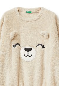 Beżowy pluszowy sweatshirt z nadrukiem twarzy misia, z haftowanymi oczami i nosem oraz małymi tridimensionalnymi uszami na ramionach. Miękka faktura.