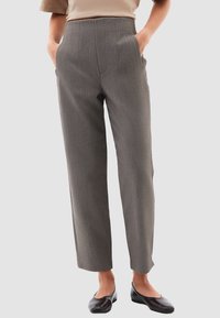 Pantalones de rayas grises con cintura alta, pierna ajustada y bolsillos laterales, confeccionados en una tela estructurada. Llevados con zapatos planos negros.