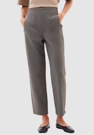 Pantalones de rayas grises con cintura alta, pierna ajustada y bolsillos laterales, confeccionados en una tela estructurada. Llevados con zapatos planos negros.