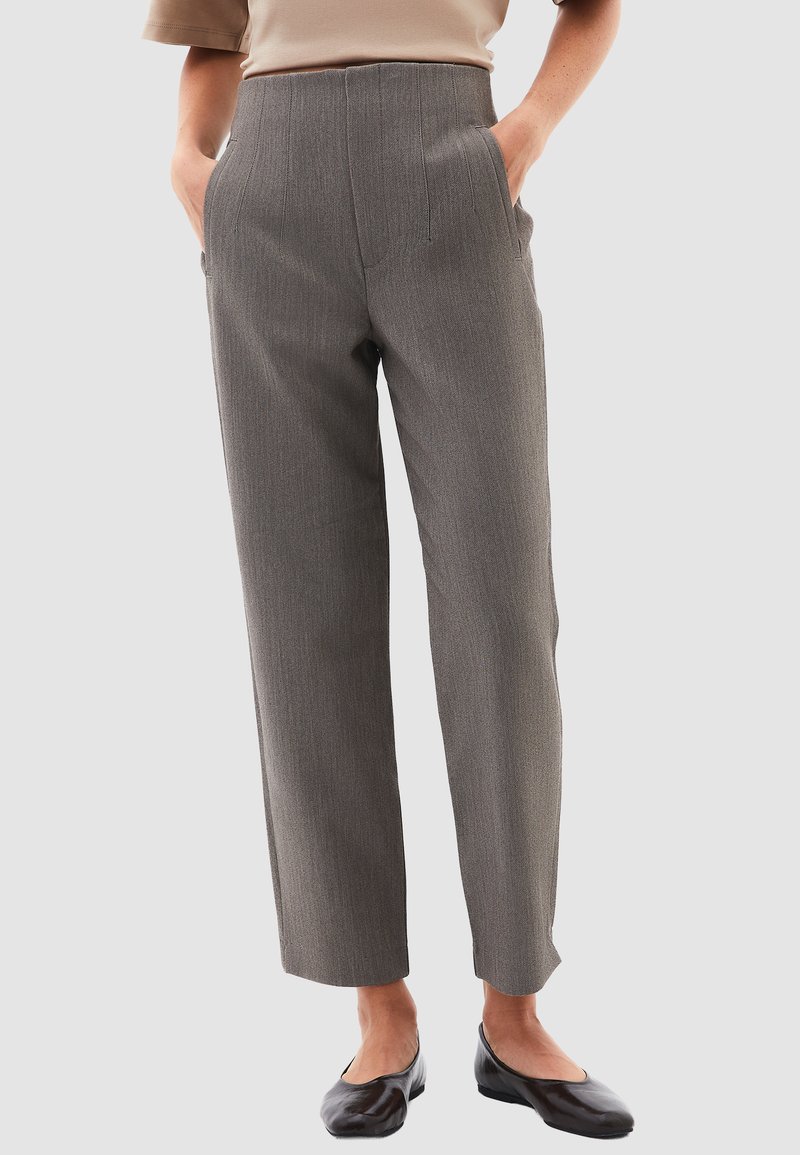 Pantalones de rayas grises con cintura alta, pierna ajustada y bolsillos laterales, confeccionados en una tela estructurada. Llevados con zapatos planos negros.