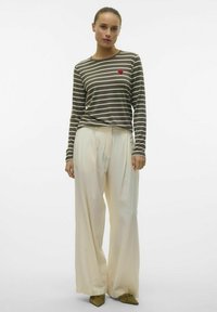 Chemise à manches longues rayée olive avec un détail de cœur rouge, associée à un pantalon large crème fluide et des chaussures vert olive.