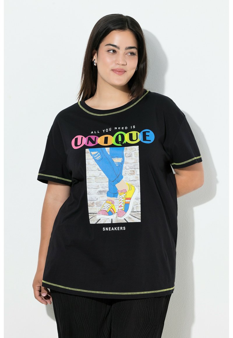 Camiseta negra de manga corta, con el texto gráfico multicolor "UNIQUE" y una ilustración de zapatillas coloridas sobre un fondo de ladrillos.