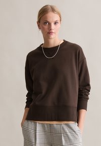 Brązowa bluza o luźnym kroju z prążkowanymi mankietami i dołem. W połączeniu z kratkami w spodniach. Gładka faktura, minimalistyczny design, okrągły dekolt.