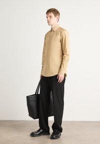 Cămașă cu maneci lungi, de culoare bej, asortată cu pantaloni negri cu croială largă și pantofi negri. Modelul poartă o poșetă mare neagră. Textura materialului este netedă.