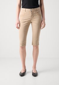 Beige kneelengde shorts laget av bomullsblanding, med klassisk fem-lommers design og knappelukking. Brukt med svarte leiligheter.