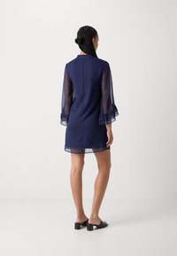 Navy blue dress with sheer layered sleeves, ruffled cuffs, and a back closure. Smooth texture, knee-length design, and minimalistic style.