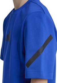 Camiseta atlética azul fabricada con una mezcla de algodón. Presenta un logotipo negro en el pecho y una franja negra con el logotipo en la manga. Manga corta, escote redondeado.