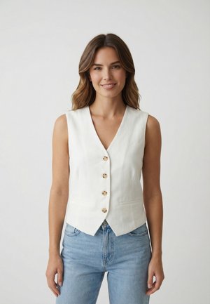 Mujer con cabello castaño ondulado, vistiendo un chaleco blanco sin mangas con botones y jeans azul claro, sonriendo frente a un fondo claro y liso.