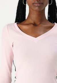 Roosa ribaga pika varrukaga pluus V-kujulise kaelusega, millel on sile tekstuur ja liibuv disain, luues sujuva silueti.