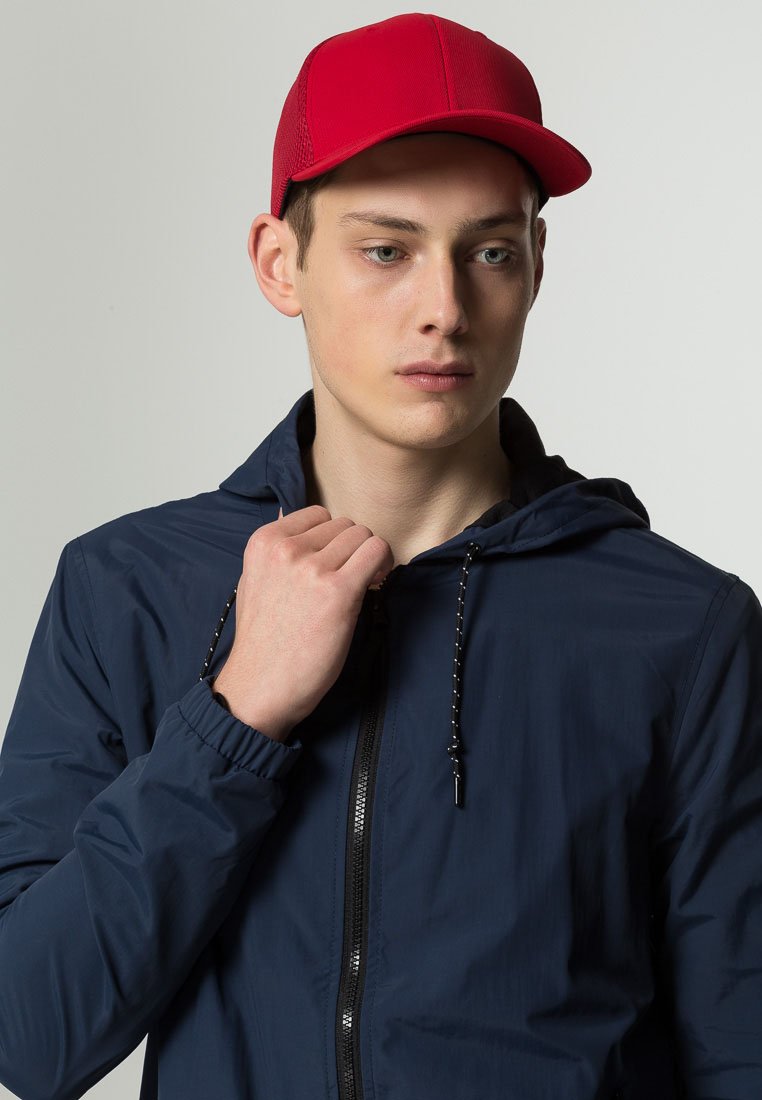 Navy windbreaker with hood and zipper, featuring elastic cuffs and drawstring. Red cap, flat brim, textured fabric, styled with a casual look.