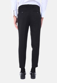 Pantaloni neri su misura con una vestibilità slim, dotati di due tasche posteriori e una trama liscia, abbinati a scarpe e calze nere.