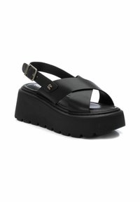 Sandalias de plataforma negras con tiras cruzadas, hechas de material sintético suave. Cuentan con una correa para el tobillo ajustable y suela acanalada.