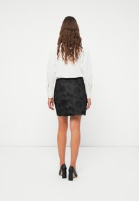Svart blommig spetskjol med en fransad kant, matchad med en vit blus med långa ärmar. Svarta högklackade skor fulländar outfiten.