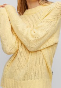 Gul stickad tröja med lös passform, ribbade muddar och nederkant, med en texturerad, öppen väv och en oversize-design.